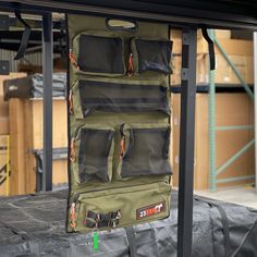 the back side of a green bag hanging on a metal rack in a warehouse with boxes and other items