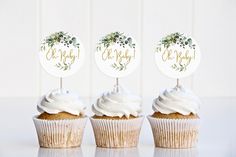 three cupcakes with white frosting and greenery on top