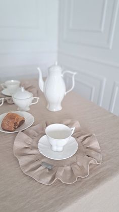 a table topped with white plates and cups filled with food next to a tea pot