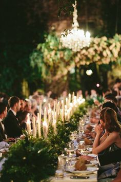 a group of people sitting at a long table with candles in the middle of it