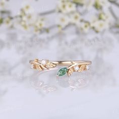 a gold ring with green leaves and white flowers in the background, sitting on top of a table