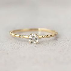 a yellow gold ring with a single diamond on the top, sitting on a white surface