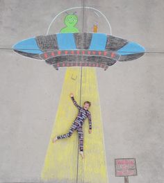 a chalk drawing of a man laying on the ground with an alien flying above him