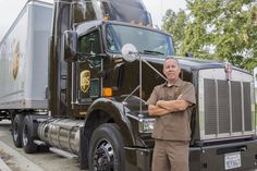 a man standing in front of a semi truck on the side of the road with his arms crossed