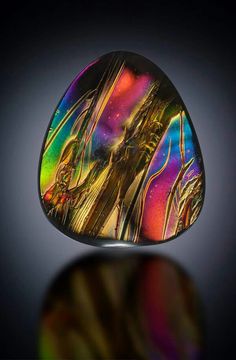 a multicolored piece of glass sitting on top of a black surface with a reflection in it