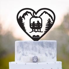 a heart shaped cake topper with a couple sitting on a bench in the mountains