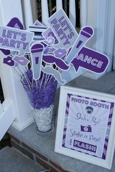 purple and white photo booth signs on the front porch with flowers in a vase next to it