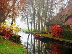 two boats are parked on the water in front of some houses and trees with autumn foliage