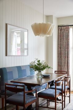 a dining room table with blue chairs and a bench in front of a window that has drapes on the windowsill