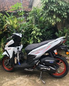 a white and red motorcycle parked in front of some bushes on the side of a road