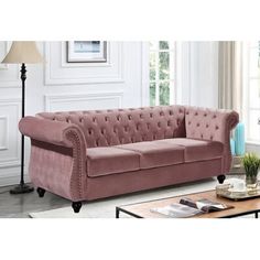 a living room with a pink velvet couch and coffee table in front of a window