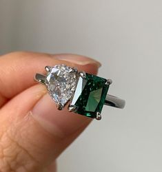 a woman's hand holding an emerald and diamond ring