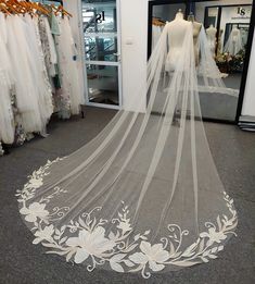 a white wedding veil with flowers on the bottom is sitting in front of a dress shop