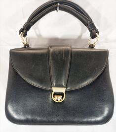 This beautiful vintage handbag from the 1950s and 1960s is made of rigid black leather and golden metal accessories. The handle is double and attaches to the bag with gold-coloured intertwined rings and, as can be seen in the photo, the lower one is damaged. The interior is lined with black eco fabric, suede effect, and there is a small tear. Suitable for parties, ceremonies, cocktails, day and evening! Made in Italy. Good condition. Measures: Width 25cm Height 18cm Thickness 10 cm Vintage Bags 1950s, Black Leather Handbag, Eco Fabric, Vintage Handbag, Metal Accessories, Black Leather Handbags, Vintage Handbags, Color Oro, Vintage Bags