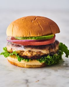 a hamburger with lettuce, tomato and onion on it sitting on a marble surface