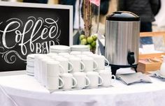 a table topped with lots of white coffee mugs next to a chalkboard sign