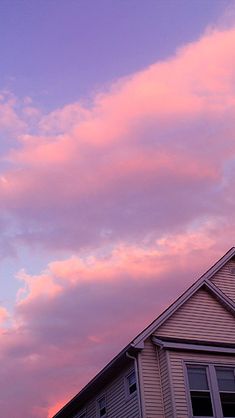 the sky is pink and purple as the sun goes down in the distance behind a house