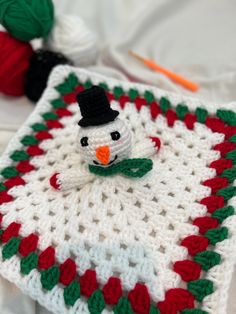 a crocheted snowman is sitting on top of a blanket with red, green and white trim