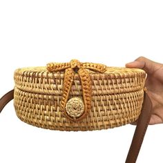 a hand holding a woven basket with a handle and brown leather strap around the bottom