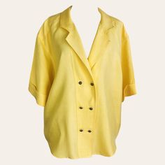 This womens stunning bright yellow double-breasted short-sleeve blouse dates back to the 1990s. The actual color is a deeper yellow than shown in the photos, as capturing the true color of clothing can be challenging. It's made from a polyester fabric with a linen-like appearance and a soft, flowing texture. A distinctive patch adorns the back panel near the center back hem, and the extended shoulders enhance the blouse's fluid silhouette. The peaked collar is integrated into the double-breasted Yellow Summer Office Tops, Casual Yellow Office Shirt, Yellow Spring Office Tops, Vintage Solid Summer Blouse, Yellow Button-up Tops For Workwear, Summer Blouse With Lapel Collar In Solid Color, Classic Yellow Button-up Tops, Retro Short Sleeve Office Top, Yellow Summer Office Shirt