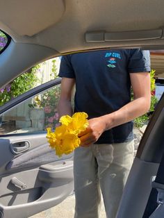 a man is holding a yellow flower in his hand while standing next to a car