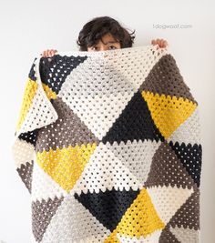 a woman is holding up a crocheted blanket