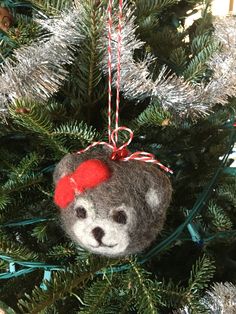 a teddy bear ornament hanging from a christmas tree with red bow on it's head