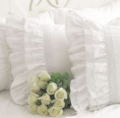 a bouquet of white roses sitting on top of a bed next to two pillows with ruffled edges