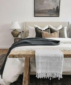 a bed with white sheets and pillows in a bedroom next to a painting on the wall