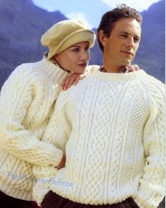 a man and woman in sweaters standing next to each other with mountains in the background