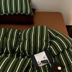 a bed covered in green and white striped sheets with a black tag on the pillow