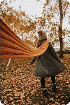 a woman is walking through the leaves with an orange scarf