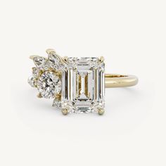 an emerald cut diamond ring with three diamonds on the band and side stones in yellow gold