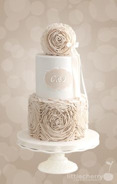 a three tiered wedding cake with roses on the top and initials on the bottom