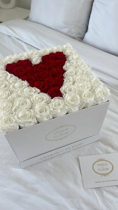 a white box with roses in the shape of a heart on top of a bed