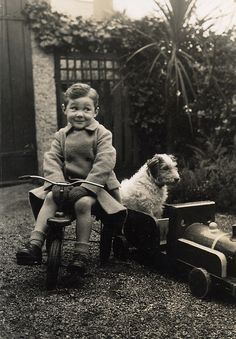 an old photo of a little boy riding a toy car with a dog on it