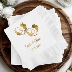 three personalized napkins on a wooden platter with white flowers and gold foil