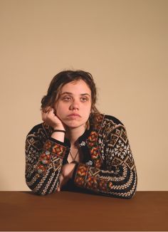 a woman sitting at a table with her hand on her chin and looking off to the side