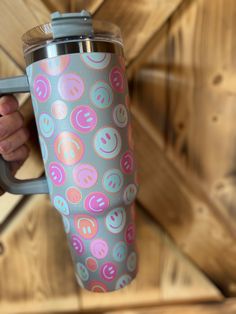 a person holding a travel mug with smiley faces on it, in front of wood planks