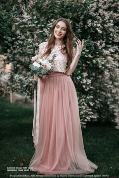 a beautiful young woman in a long pink dress posing for the camera with her bouquet