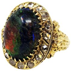 Truly incredible black opal and diamond cocktail ring with bold, vibrant colors. This rare, vintage piece is a visual showstopper with its iridescent play-of-color and sparking diamonds, while the ornately carved gold shank adds to the charm of this stunning ring. The gorgeous black opal stone is an impressive 8.79 carats with a unique multi-color tone. It is a prong set oval cabochon stone surrounded at the base by a halo of 16 natural round rose cut diamonds (J-K / VS1-VS2I) totaling .42 carat Black Opal Stone, Diamond Cocktail Ring, Jewelry Appraisal, Gold Cocktail Ring, Gold Cocktail, Diamond Cocktail Rings, Opal Stone, White Gold Engagement Rings, Pretty Rings