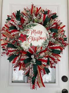 a christmas wreath on the front door is decorated with red, white and green ribbons