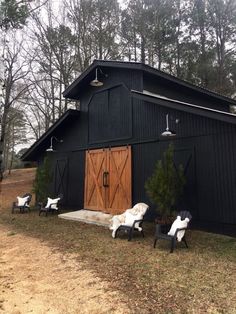 three lawn chairs sitting in front of a black barn with wooden doors and windows on the side