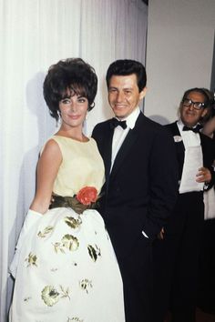 a man and woman standing next to each other in formal wear, posing for the camera