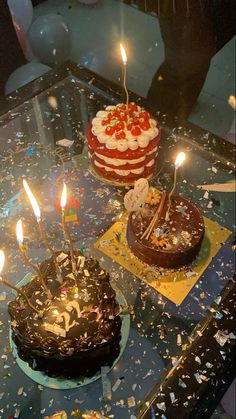 two cakes with lit candles on them sitting on top of a glass table covered in confetti and sprinkles