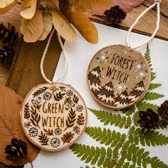 two wooden ornaments that say forest witch and green witch with pine cones in the background