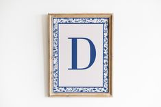 a blue and white frame hanging on the wall with a letter d painted on it