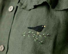 a black bird sitting on top of a tree branch embroidered onto a green button up shirt