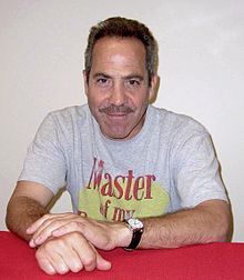 a man sitting at a red table with his hand on the top of it and smiling