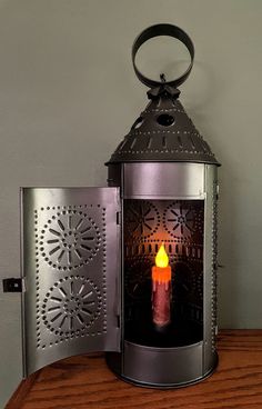 a lit candle sitting inside of a metal lantern on top of a wooden table next to a wall